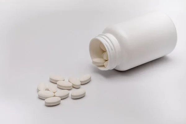 Białe okrągłe tabletki pokryte osłoną są rozrzucone z plastikowej puszki razem z nimi. Narkotyki, pigułki. — Zdjęcie stockowe