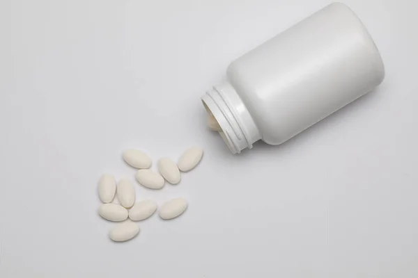 Białe okrągłe tabletki pokryte osłoną są rozrzucone z plastikowej puszki razem z nimi. Narkotyki, pigułki. — Zdjęcie stockowe