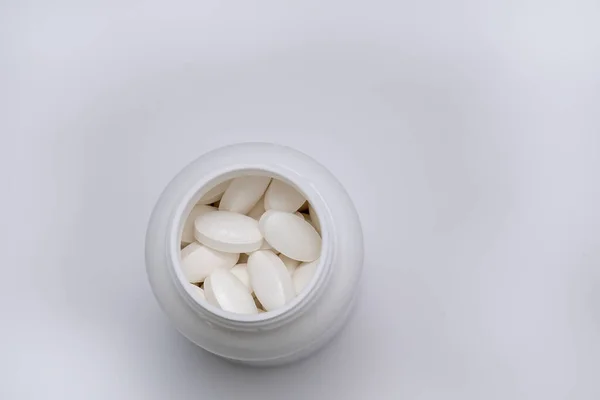 Duże, okrągłe i lekkie tabletki. Białe okrągłe tabletki pokryte osłoną są rozrzucone z plastikowej puszki razem z nimi. . — Zdjęcie stockowe