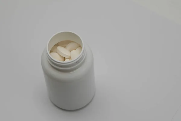 Os comprimidos redondos brancos cobertos com uma cobertura espalham-se de uma lata plástica com eles. Drogas, pílula . — Fotografia de Stock