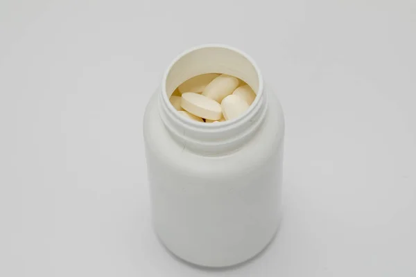 Witte ronde tabletten bedekt met een omslag worden met hen uit een plastic blik gestrooid. Drugs, pil. — Stockfoto