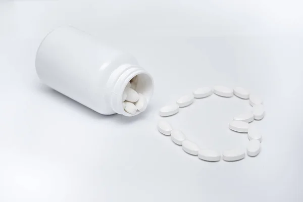 Białe okrągłe tabletki w kształcie serca leżą w białym słoiku i są rozrzucone wokół — Zdjęcie stockowe