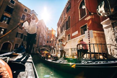 İtalya 'nın Venedik caddesinde gondolculuk yaparken iki yakışıklı gondolcu. Gondolcular ellerinde telefonlar, gondollarda oturuyorlar..