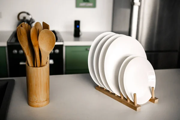 wooden kitchen utensils in a wooden glass on the background of a beautiful modern kitchen White shelving unit with set of dishware