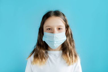 Koronavirüs pandemisi sırasında antiviral koruma. Mavi arka planda tıbbi maske takan genç bir kızın portresi. Solunum koruması