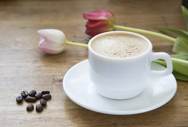 White cup with latte coffee and flowers on a wooden table