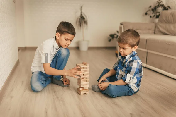 İki erkek kardeş evin zeminine ahşap bloklardan bir kule inşa ediyorlar. Masa oyunu. Bağımsız aile karantinası, enfeksiyon, koronavirüs, kendini izole etme kavramı..