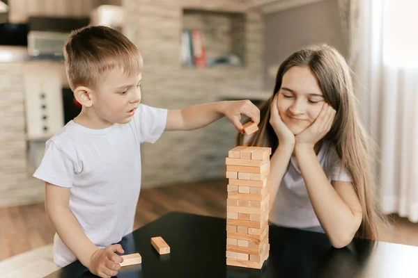 Erkek ve kız kardeş evde ahşap bloklardan bir kule inşa ediyorlar. Masa oyunu. Bağımsız aile karantinası, enfeksiyon, koronavirüs, kendini izole etme kavramı. Evde kal. Seçici odak