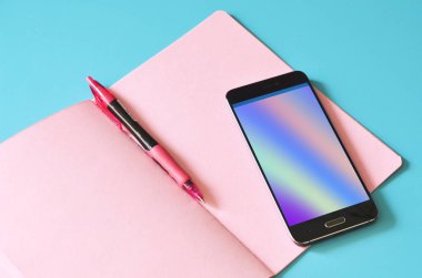 Soyut holografik akışına sahip akıllı telefon ekranda, pembe defter mavi masada. Tasarım için hazırlan