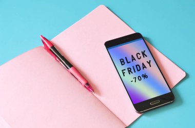 Soyut holografik akış üzerine Kara Cuma indirimli akıllı telefon ve mavi masadaki pembe defter. Tasarım için hazırlan