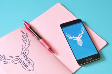 Yılbaşı yağmuru geyiği sergilenen akıllı telefon ve mavi masada pembe defter. Tasarım için hazırlan