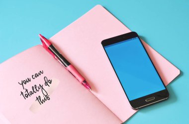 Akıllı telefon ve pembe defter. Bunu mavi masada yapabilirsin. Tasarım için hazırlan