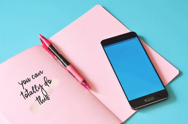 Akıllı telefon ve pembe defter. Bunu mavi masada yapabilirsin. Tasarım için hazırlan