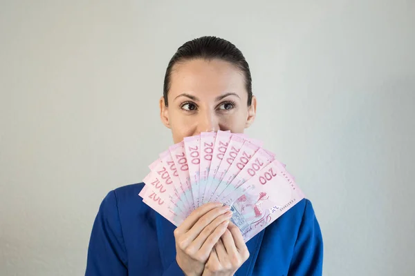 Здивована жінка в класичній синій куртці тримає українці банкноти біля обличчя. — стокове фото