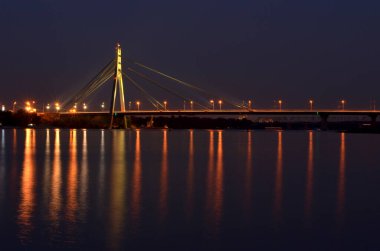 Gece Dnipro nehrinin kıyısında suda yansıyan bir köprü.