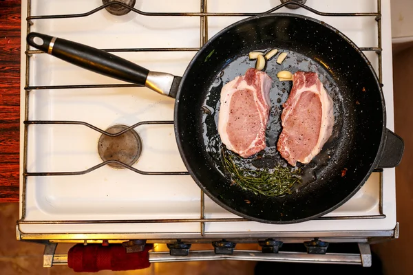 Daging babi mentah steak dengan rempah-rempah dalam wajan, memasak makanan di dapur rumah — Stok Foto
