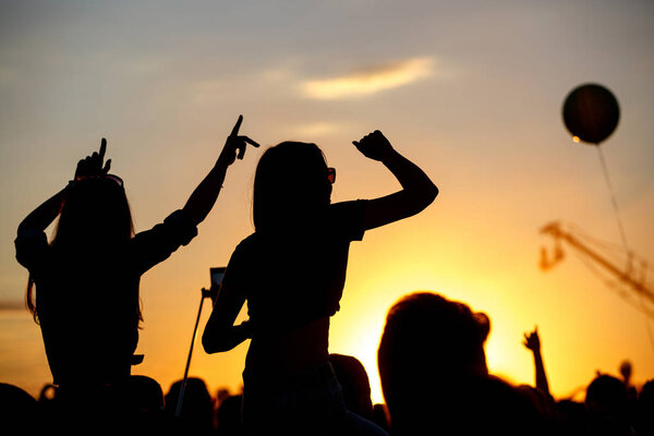 Girls with hands up dancing, singing and listening the music during concert show on summer music festival, sunset