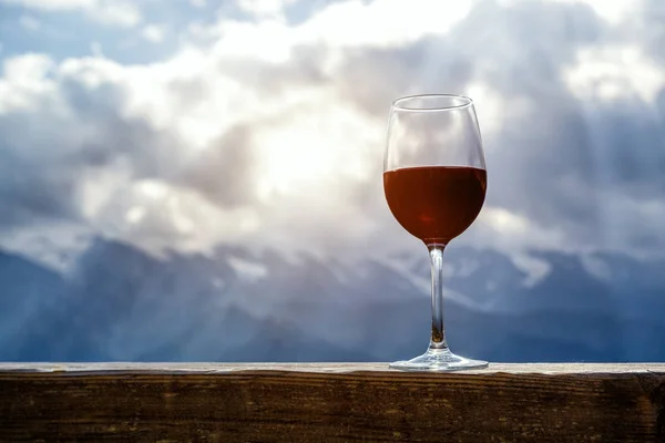 Бокал красного вина на пикнике, стоящий на деревянном столе на фоне красивых гор — стоковое фото