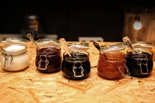 Vasi di vetro con diversi tipi di marmellata e bacche su tavolo di legno — Foto Stock
