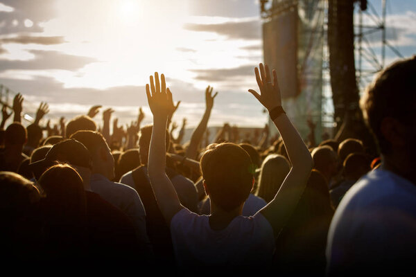 Teenagers at summer music festival enjoying themselves, raised hands, sunset