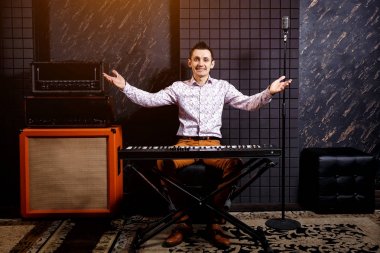 Bir müzisyen bir ışık gömlekli bir piyano synthesizer bir karanlık kayıt stüdyosunda çalış..