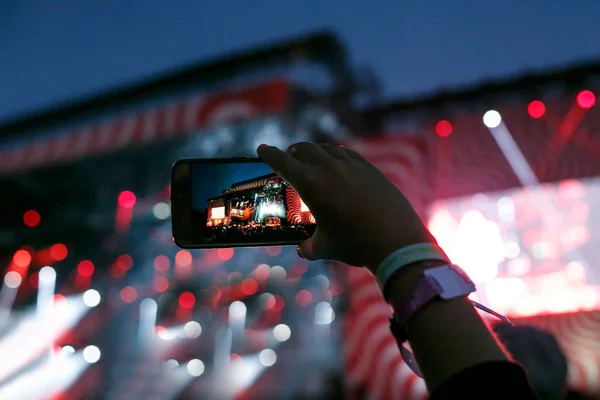 Mano con uno smartphone registra musica dal vivo festival e scattare foto del palco del concerto . — Foto Stock