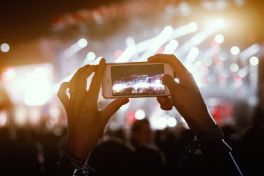 Ellerinde akıllı telefon kayıtları olan canlı müzik festivali, konser sahnesinin fotoğrafını çekiyor.