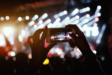 Ellerinde akıllı telefon kayıtları olan canlı müzik festivali, konser sahnesinin fotoğrafını çekiyor.