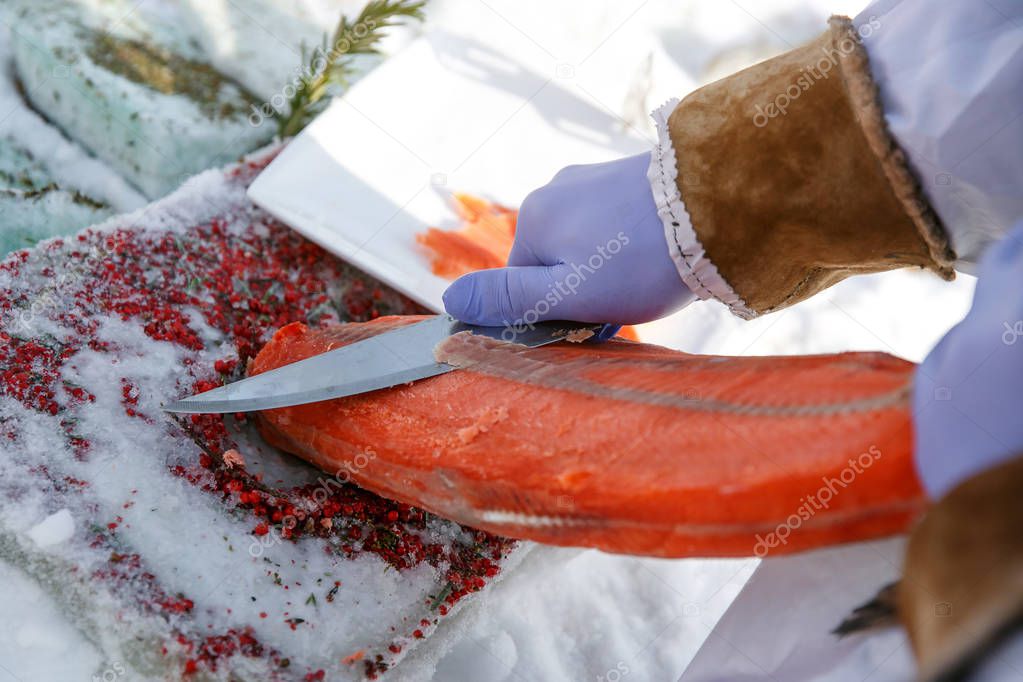 Cutting frozen fish, salmon, on fillets. Red kitchen board, hands in special blue gloves