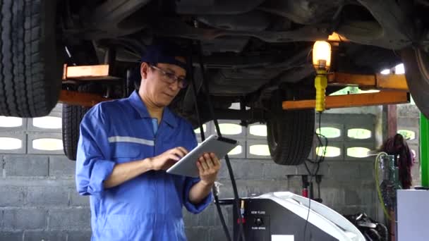 身穿蓝色制服的技工站在车下 在汽车维修车间工作 — 图库视频影像