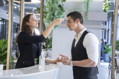 Tezgahtaki görevli kadın, binadaki ziyaretçilerin sıcaklığını ölçmek için dijital termometreyi kullandı. Ateşli insanları, Covid 19 konseptini,