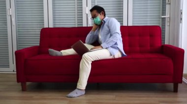 Asyalı adamlar tıbbi maske takarlar. Yorgunum. Evdeki kırmızı kanepede uyumaya çalış. Karantinaya al ve evde kal..