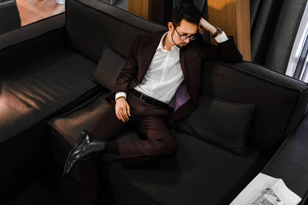 man in an expensive classic suit sitting on a sofa with a glass of whiskey