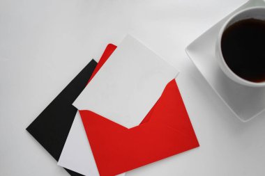  İyi sabahlar. Beyaz bir masada kırmızı bir zarfın içinde kartpostal. Beyaz bardakta kahve..                              