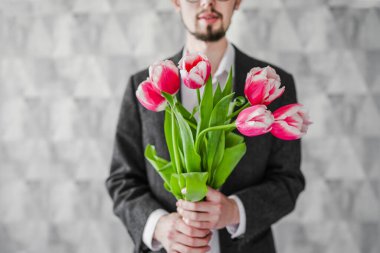 Elinde bir buket çiçekle bir adam. Kutlama. Bir erkek lale verir..
