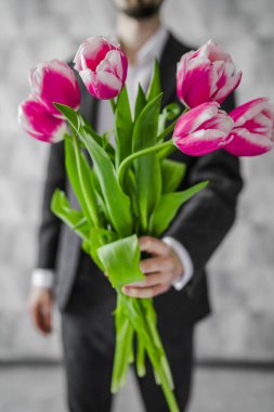 Elinde bir buket çiçekle bir adam. Kutlama. Bir erkek lale verir..
