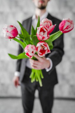 Elinde bir buket çiçekle bir adam. Kutlama. Bir erkek lale verir..