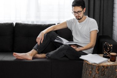 Adam kanepede dinleniyor ve evde kitap okuyor..