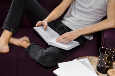 Adam kanepede dinleniyor ve evde kitap okuyor..