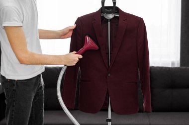 Bir adam işleri yoluna koyar. Buhar makinesini elinde tutuyor ve yıkadıktan sonra ceketi düzleştiriyor.