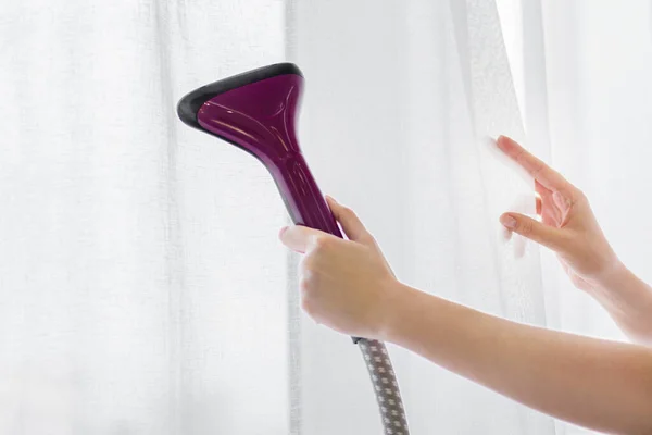 The girl holds a steamer for curtains in her hand. Cleaning of the apartment. macro