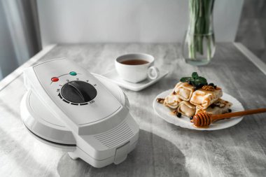 Krep ve çayın olduğu bir masada waffle ızgarası. panini presi