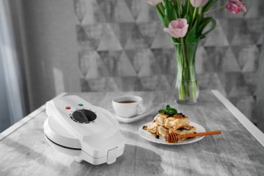 Krep ve çayın olduğu bir masada waffle ızgarası. panini presi