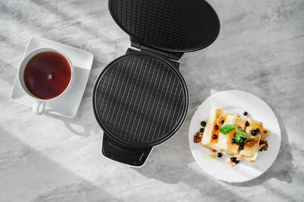 Krep ve çayın olduğu bir masada waffle ızgarası. panini presi