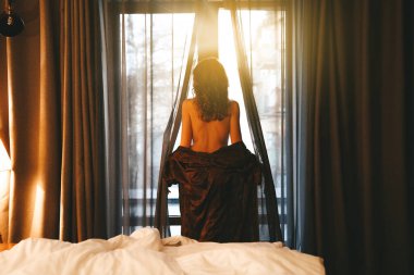 Bir kadın yatak odasının penceresinden şafakla tanışır, uzun ipek bir sabahlıkla perdeleri açar