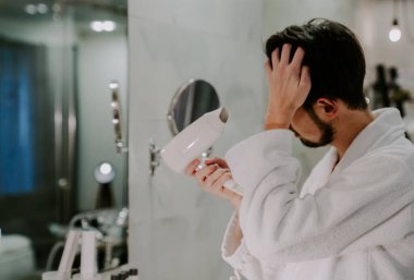 Beyaz önlüklü duştan sonra mutlu bir adam saçını kurutur. sabah spa tedavileri.