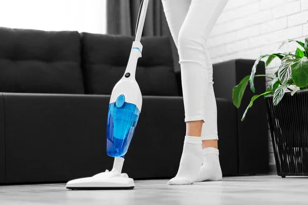 a woman in white cleans the floor with a hand vacuum cleaner. General cleaning of the house. Housewife is putting things in order. cleaning services