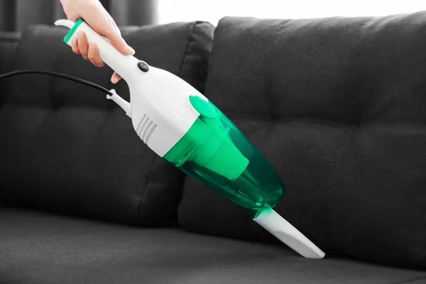 woman cleans the sofa with a hand vacuum cleaner. General cleaning of the house. Housewife is putting things in order. cleaning services