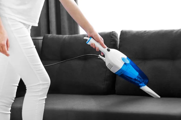 woman cleans the sofa with a hand vacuum cleaner. General cleaning of the house. Housewife is putting things in order. cleaning services