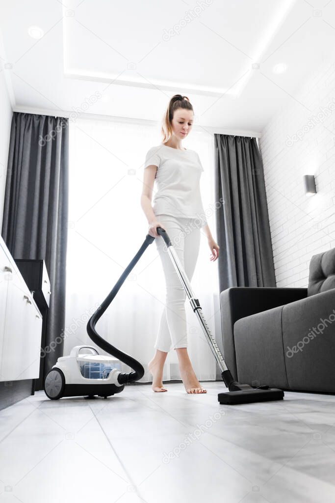 a woman in white is cleaning the floor with a vacuum cleaner. General cleaning of the house. Housewife is putting things in order. cleaning services